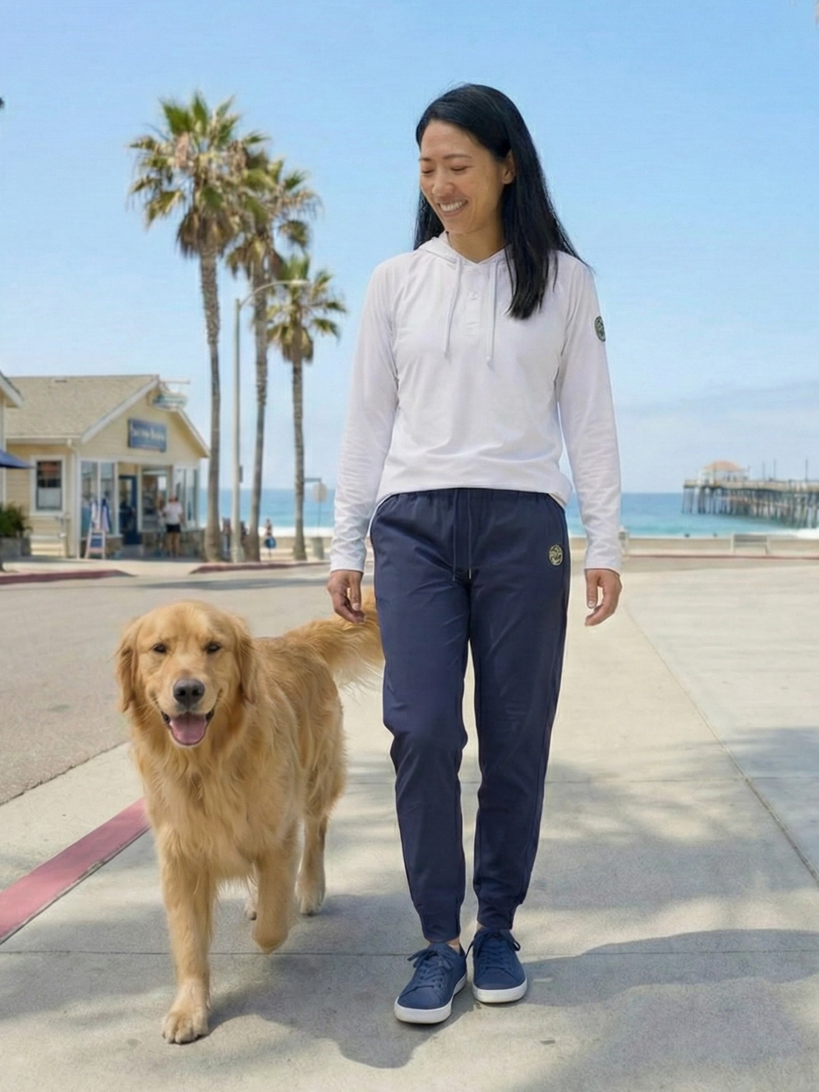 Woman walking golden retriever in navy joggers at beach